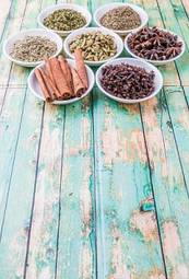 Fototapeta cardamom, star anise, cinnamon, clove, coriander seed spices and parsley, thyme, rosemary herbs in white bowls