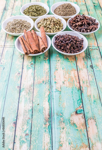 Fotoroleta Cardamom, star anise, cinnamon, clove, coriander seed spices and parsley, thyme, rosemary herbs in white bowls